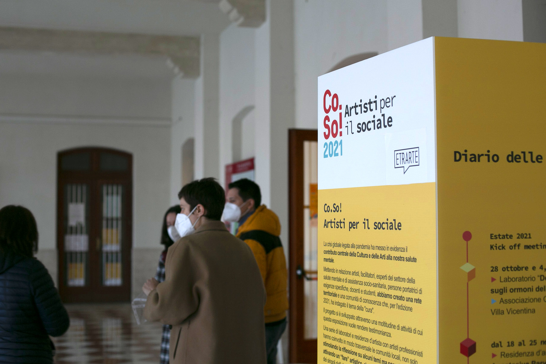 Persone con mascherina parlano accanto a cartonato di spiegazione del progetto Co.So.