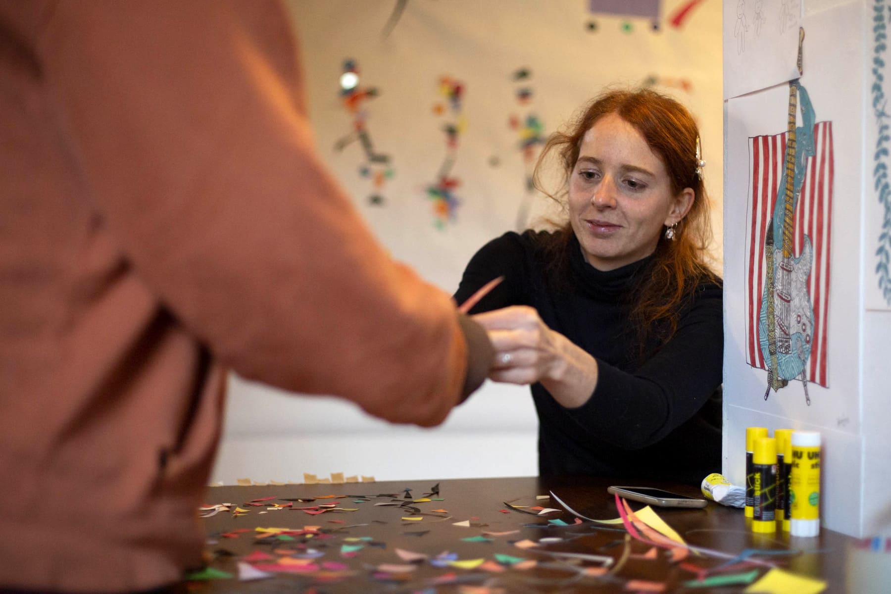 L'artista Carolina Pozzi aiuta una ragazza a ritagliare piccoli pezzi di carta colorata.