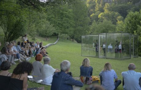 Un gruppo di ballerini danza in un cubo di vetro davanti ad un pubblico.