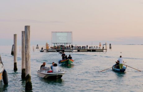 Laguna di Venezia al tramonto con barchette che si dirigono verso il Cinema galleggiante.